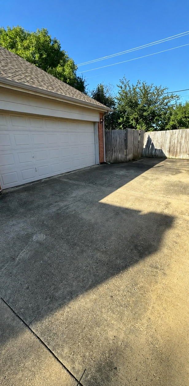 Driveway beside a white garage, wooden fence, and dry yard under a clear blue sky