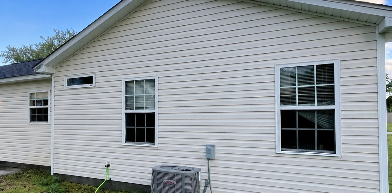 White vinyl house exterior with several windows and a small utility unit along the side yard