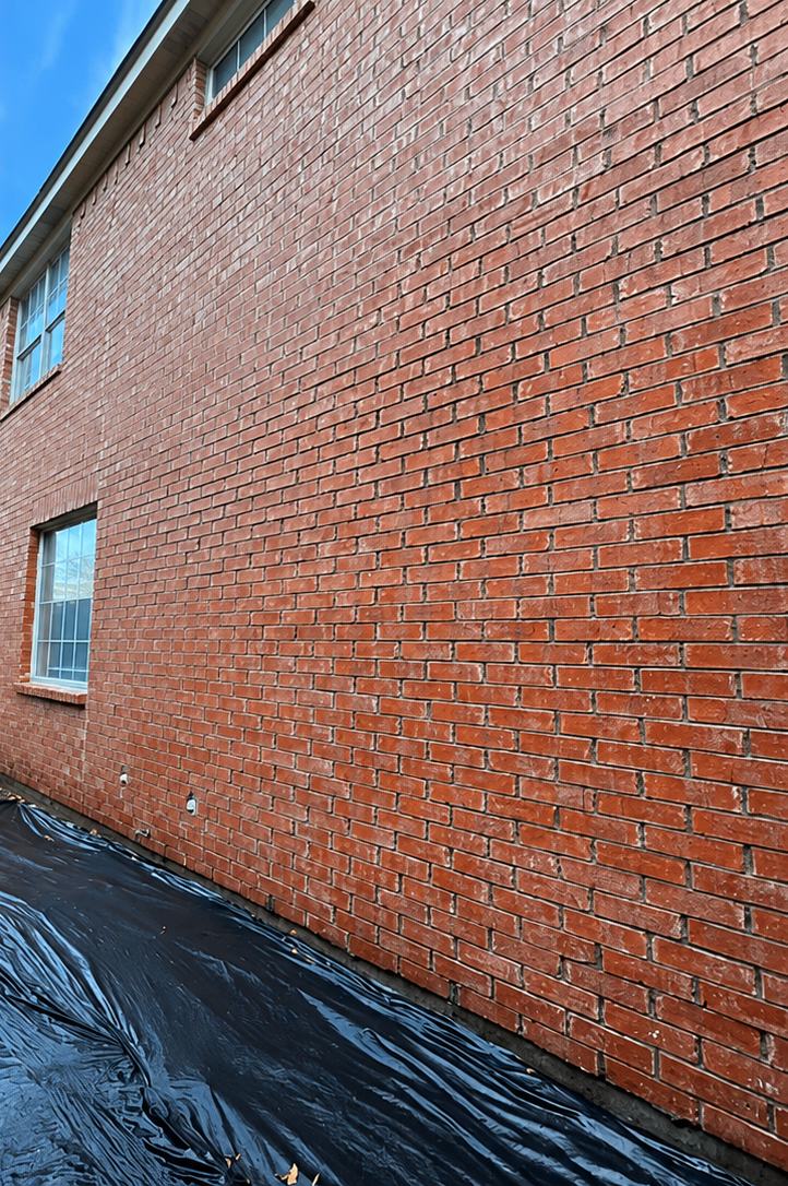Red brick wall beside a black tarp-covered ground, with a small blue window on the left.