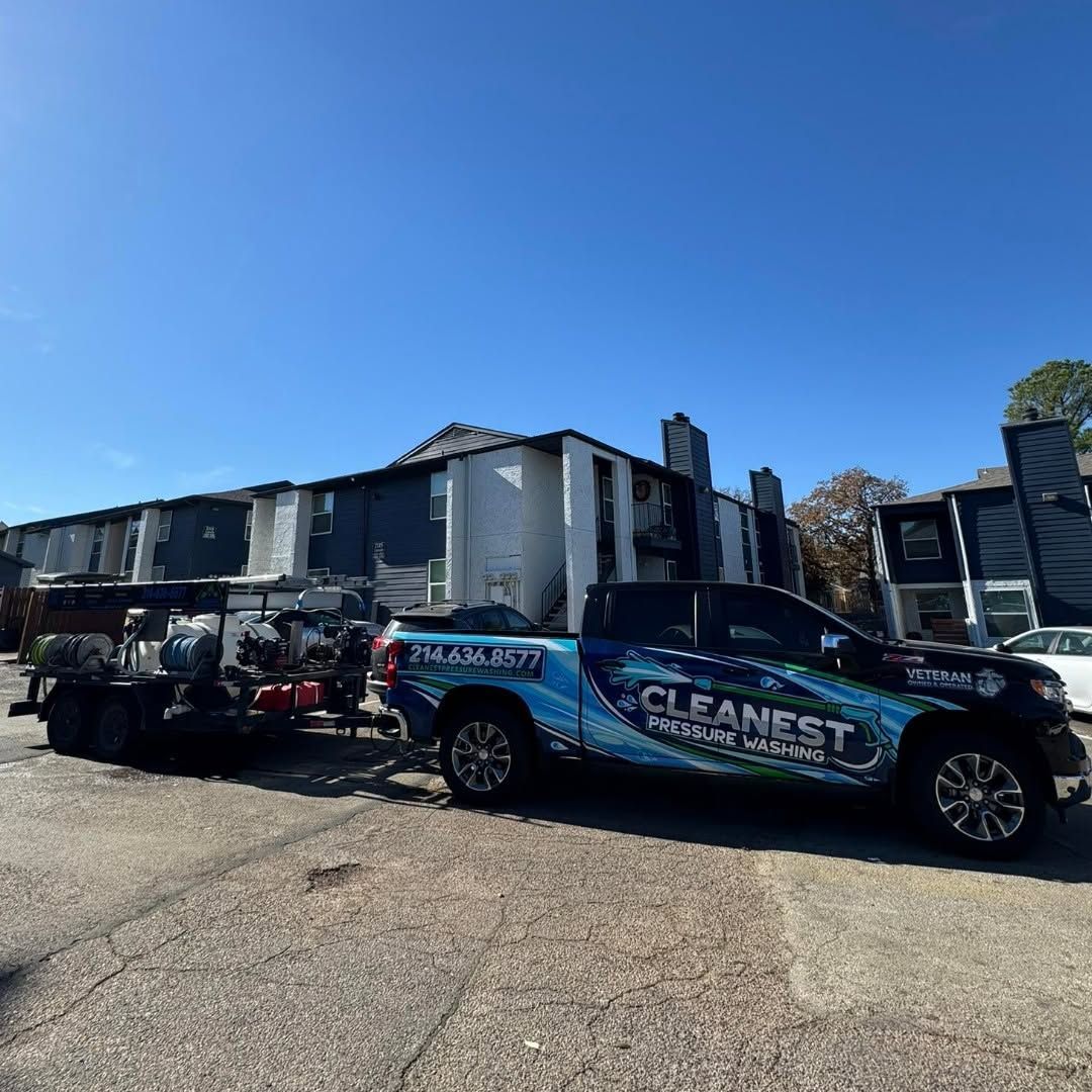 Black pickup with trailer advertising “CLEANEST” parked outside apartment buildings on a sunny day