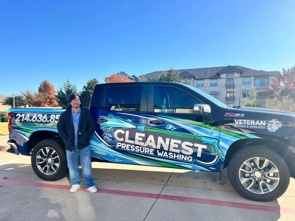 Woman standing beside a black pickup truck wrapped in blue-green “CLEANEST” pressure washing advertising.
