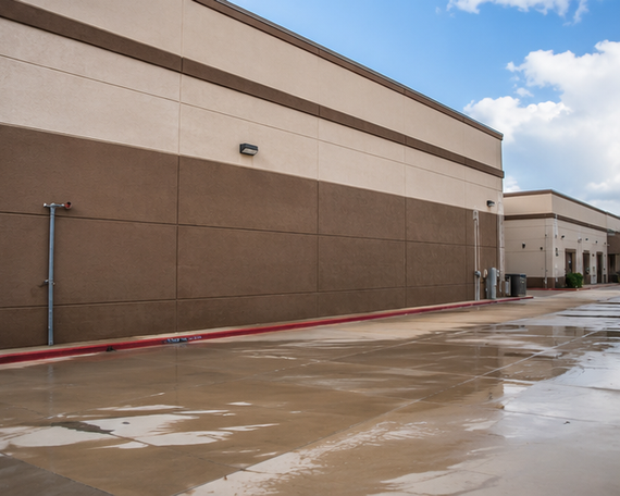 Wet parking lot beside a beige commercial building under a cloudy sky