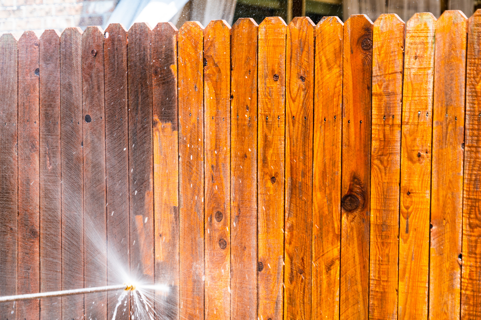 Water spraying a weathered wooden fence, with dark and orange stained boards.