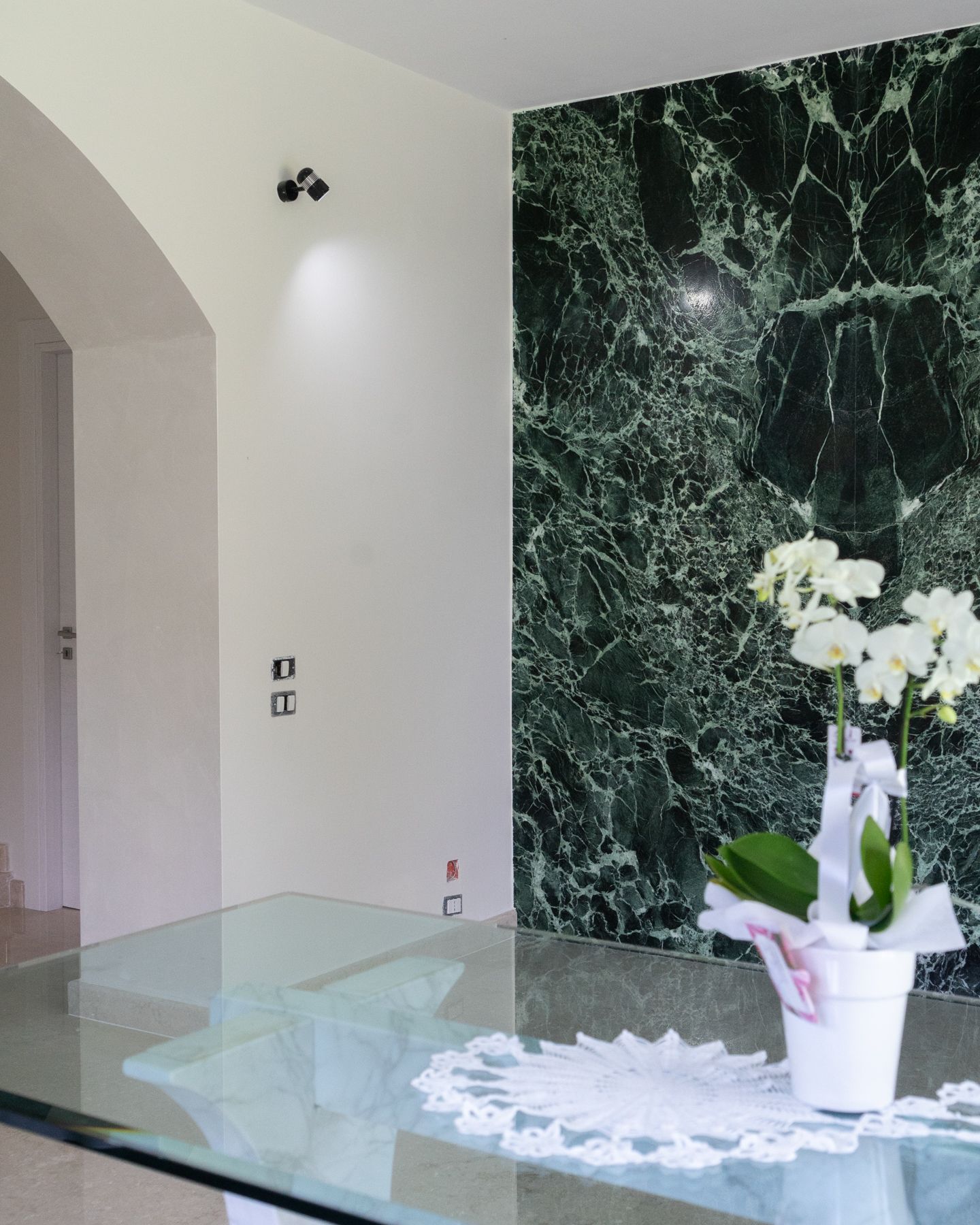 Interno con parete in marmo verde, orchidee bianche e porta ad arco.