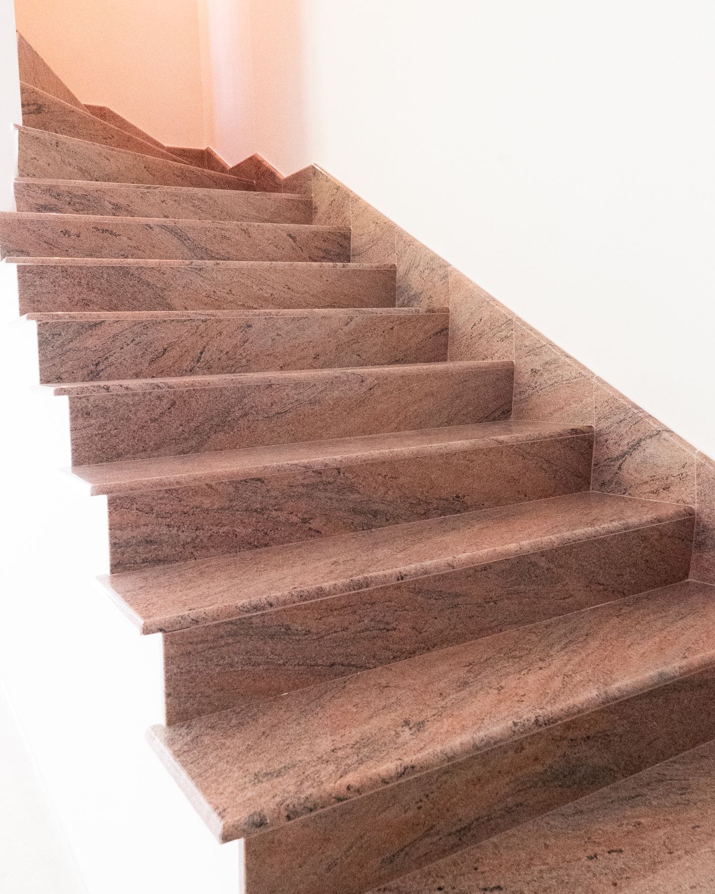 Scala in granito rosso contro una parete bianca.