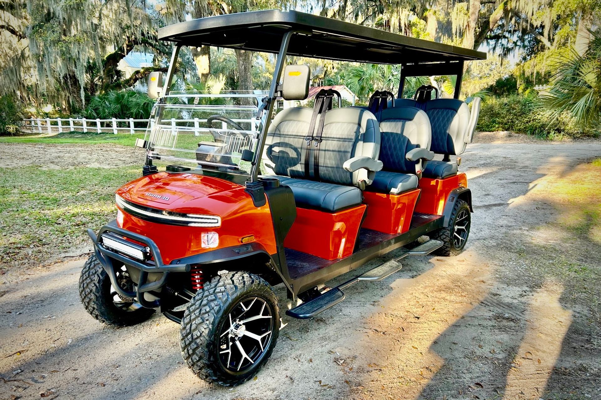 Red six-seater golf cart with black roof and custom wheels parked on a gravel road in front of trees.
