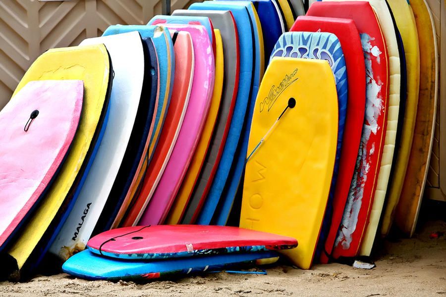 Pile of colorful boogie boards leaning against a wall on sand.