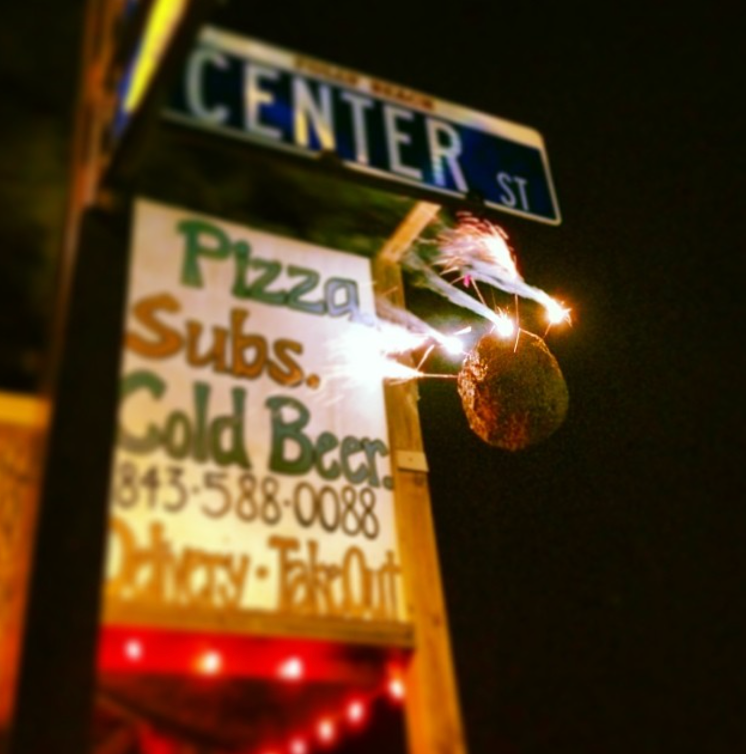 Sign for Center Street pizzeria with sparks flying from a coconut, at night.