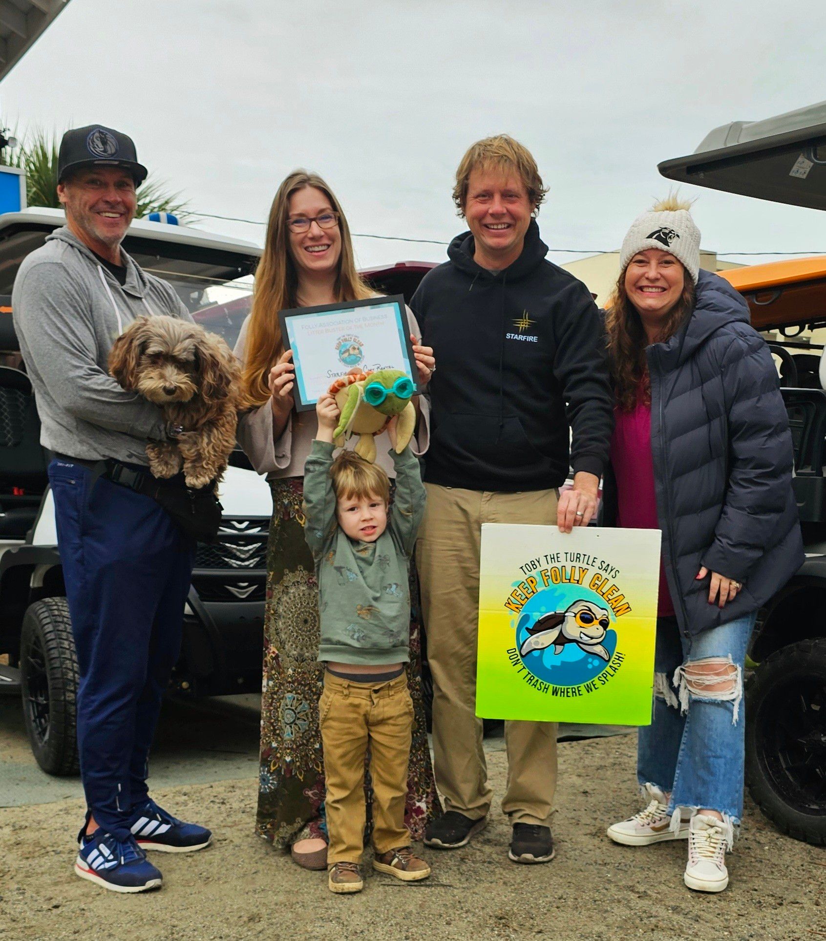 Group of five people, a dog, and a child holding a stuffed animal pose with a certificate.