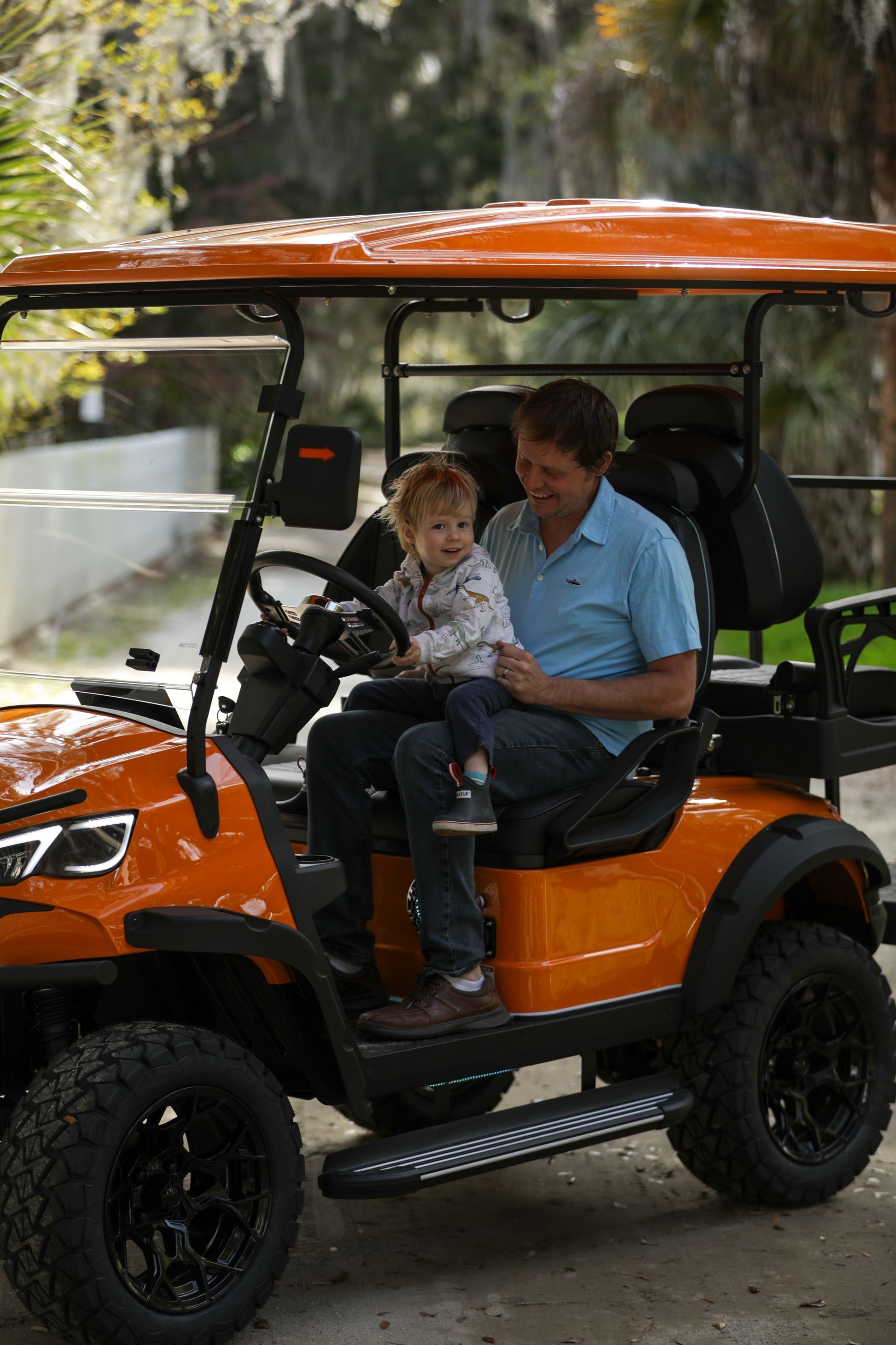 A man and a young child sit in an orange golf cart.