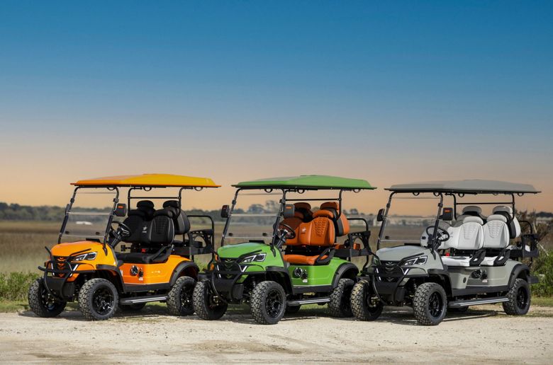 Three colorful, off-road golf carts parked in front of a rural landscape under a blue sky.