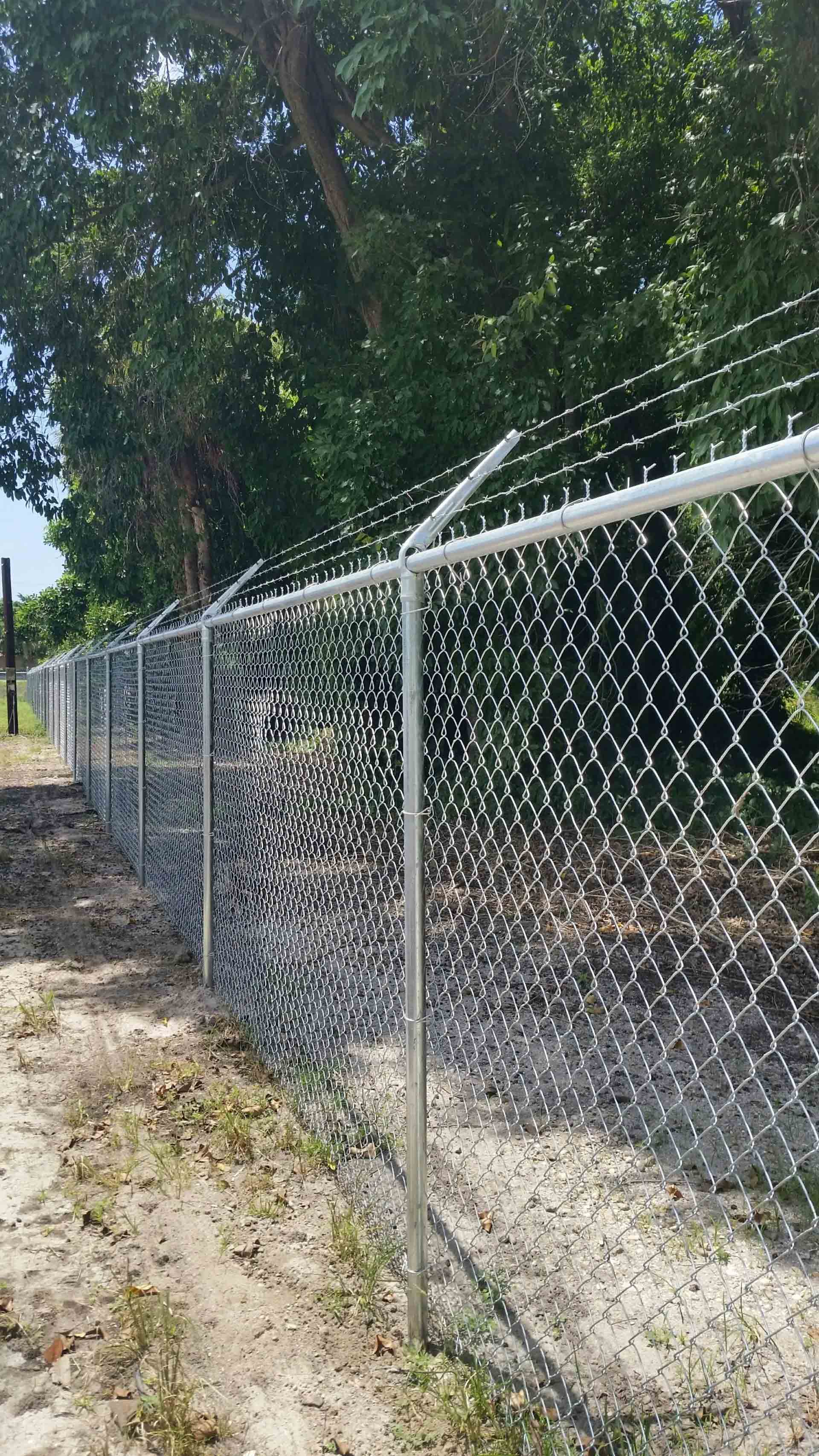 A chain link fence is surrounded by trees and dirt.