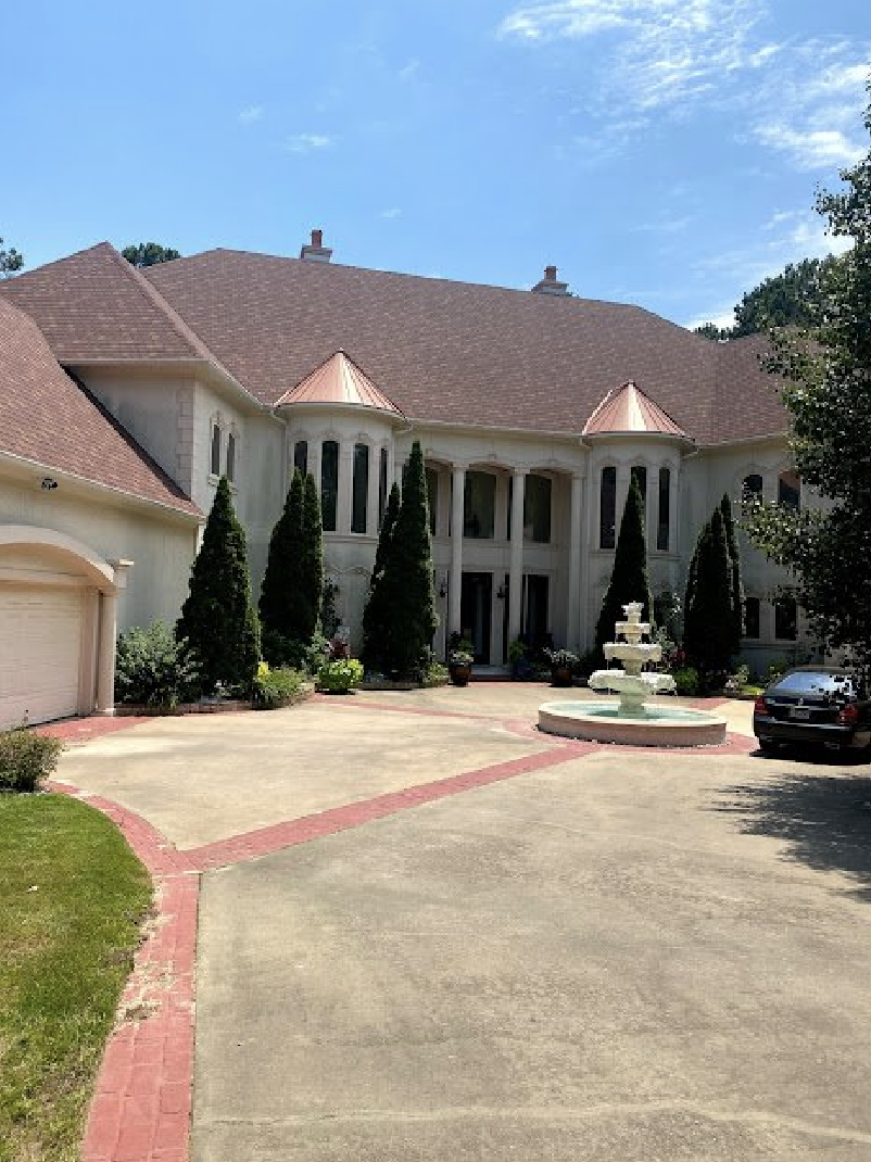 A large white house with a red roof and a fountain in front of it.