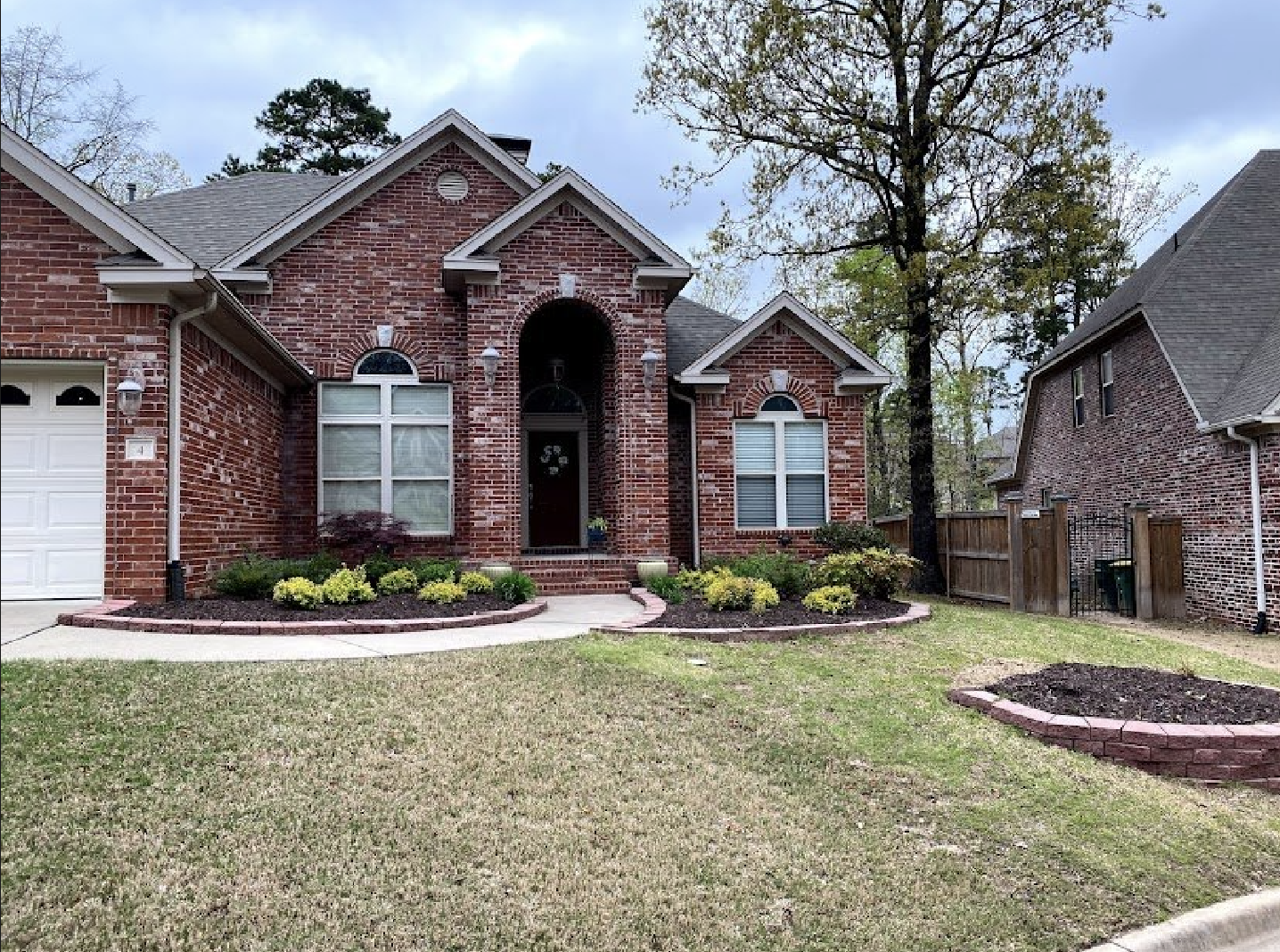 A brick house with a white garage door and a lush green lawn in front of it.