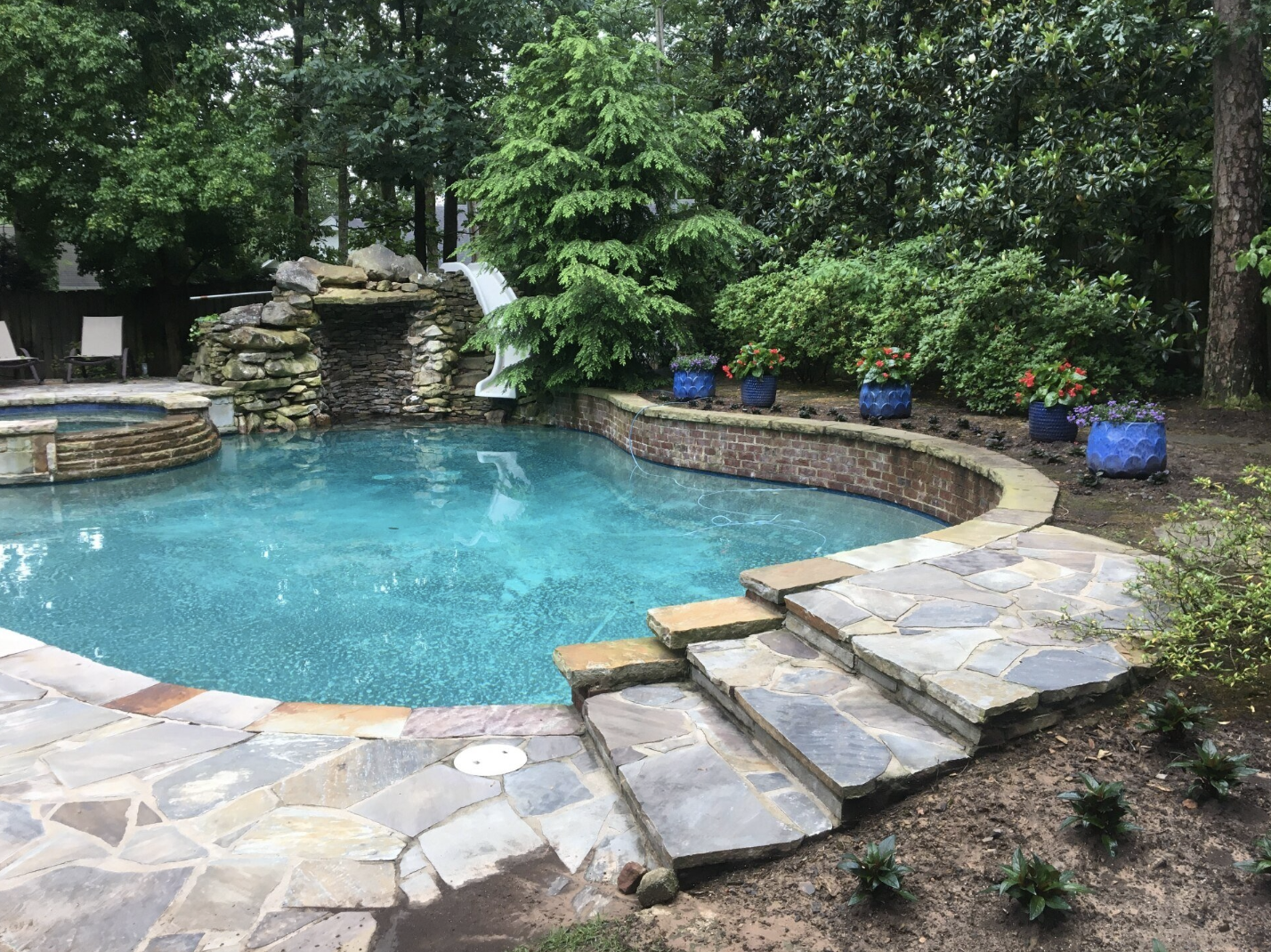 A large swimming pool with stairs and a waterfall in the backyard.