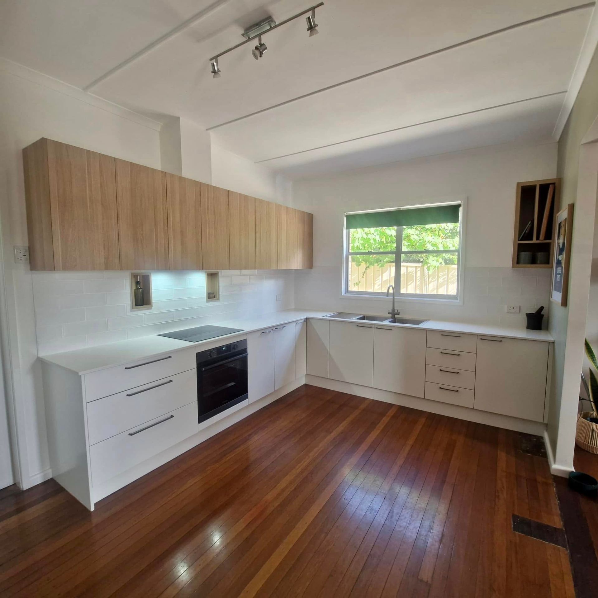 A kitchen with wooden floors and white cabinets and a window — Coastal Detail Joinery in Tuncurry, NSW