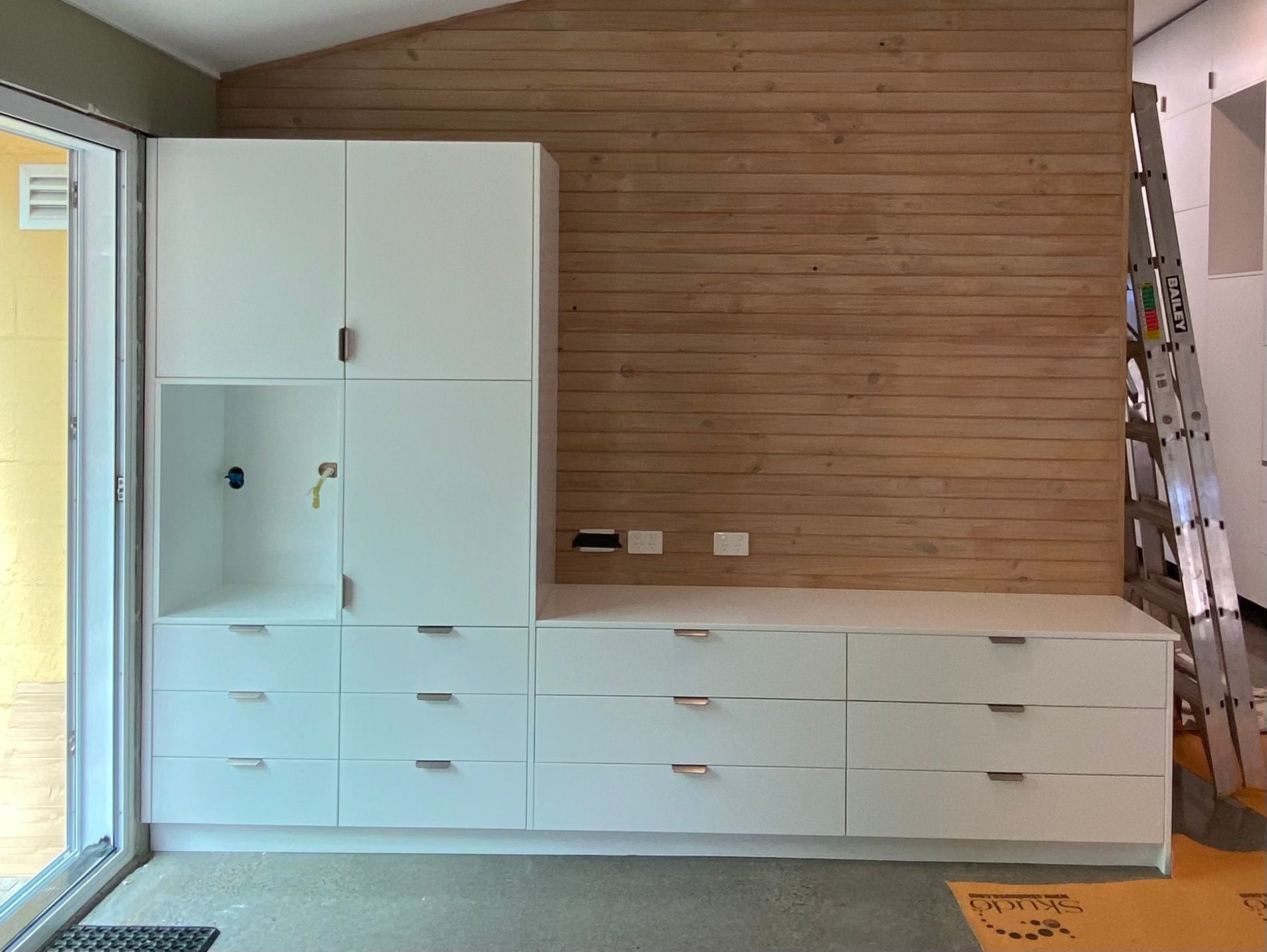 A room with white cabinets and drawers and a wooden wall — Coastal Detail Joinery in Tuncurry, NSW