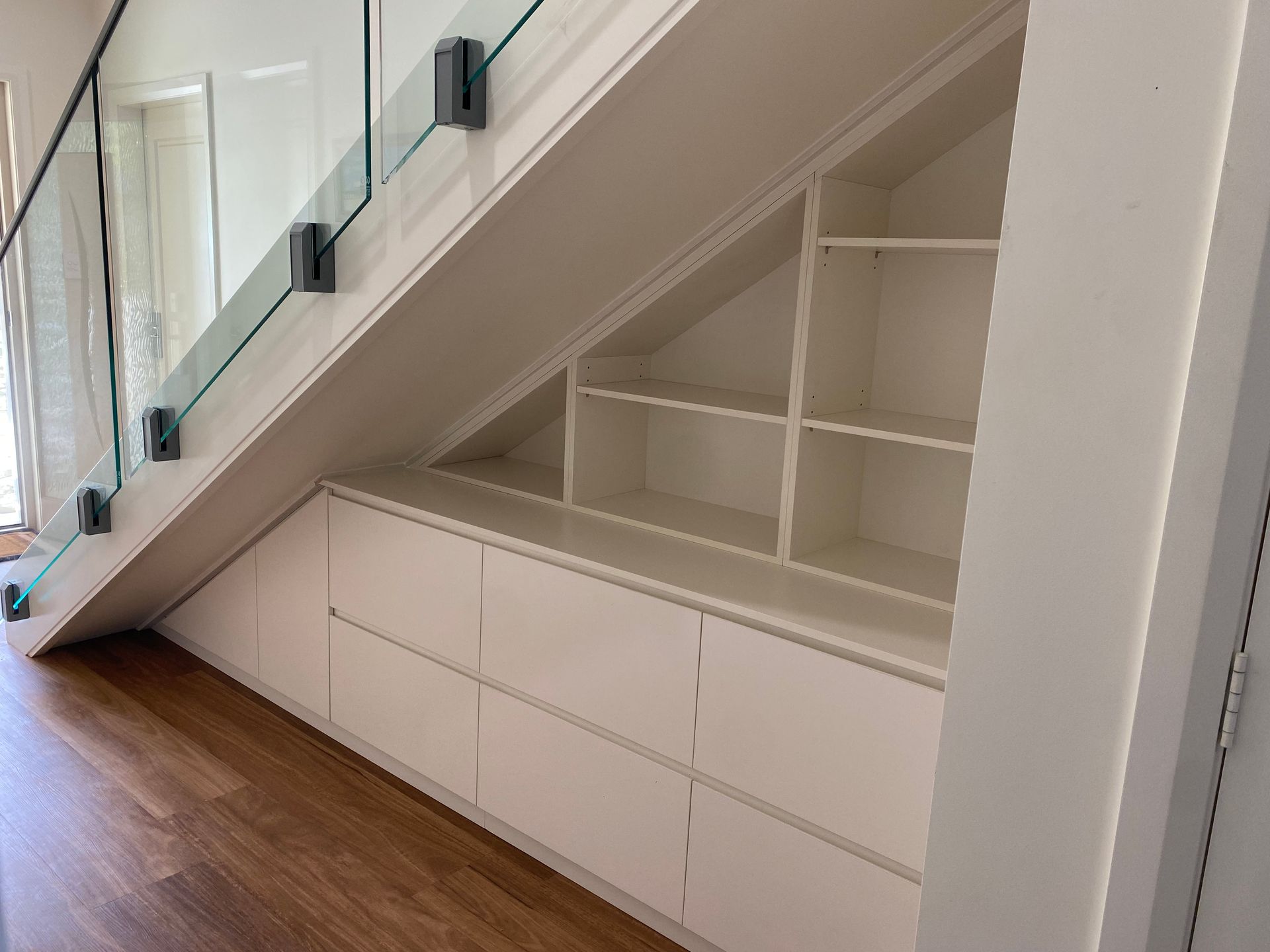 A staircase with a glass railing and a built in shelf underneath it — Coastal Detail Joinery in Tuncurry, NSW