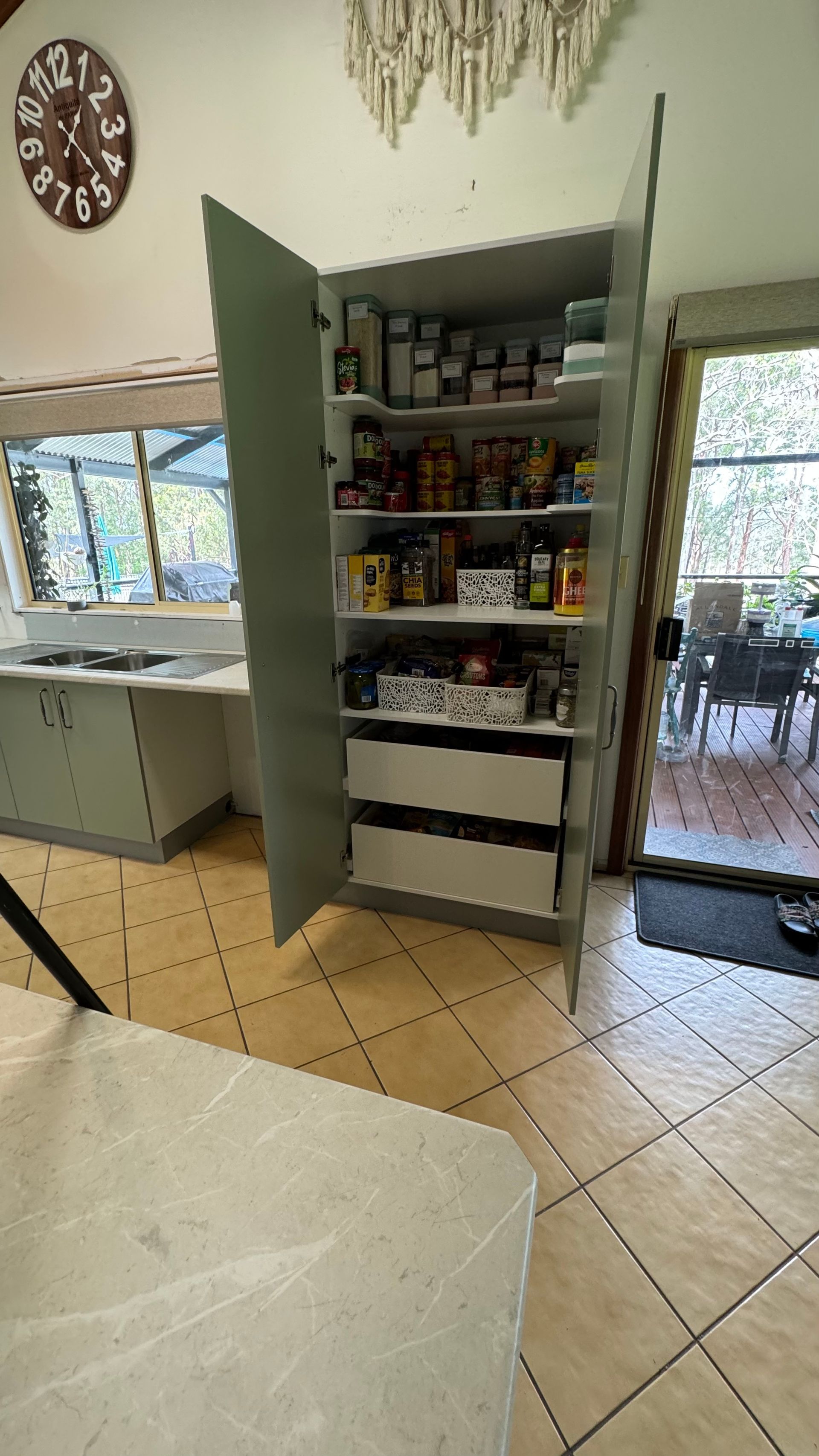A kitchen with a pantry and a clock on the wall — Coastal Detail Joinery in Tuncurry, NSW