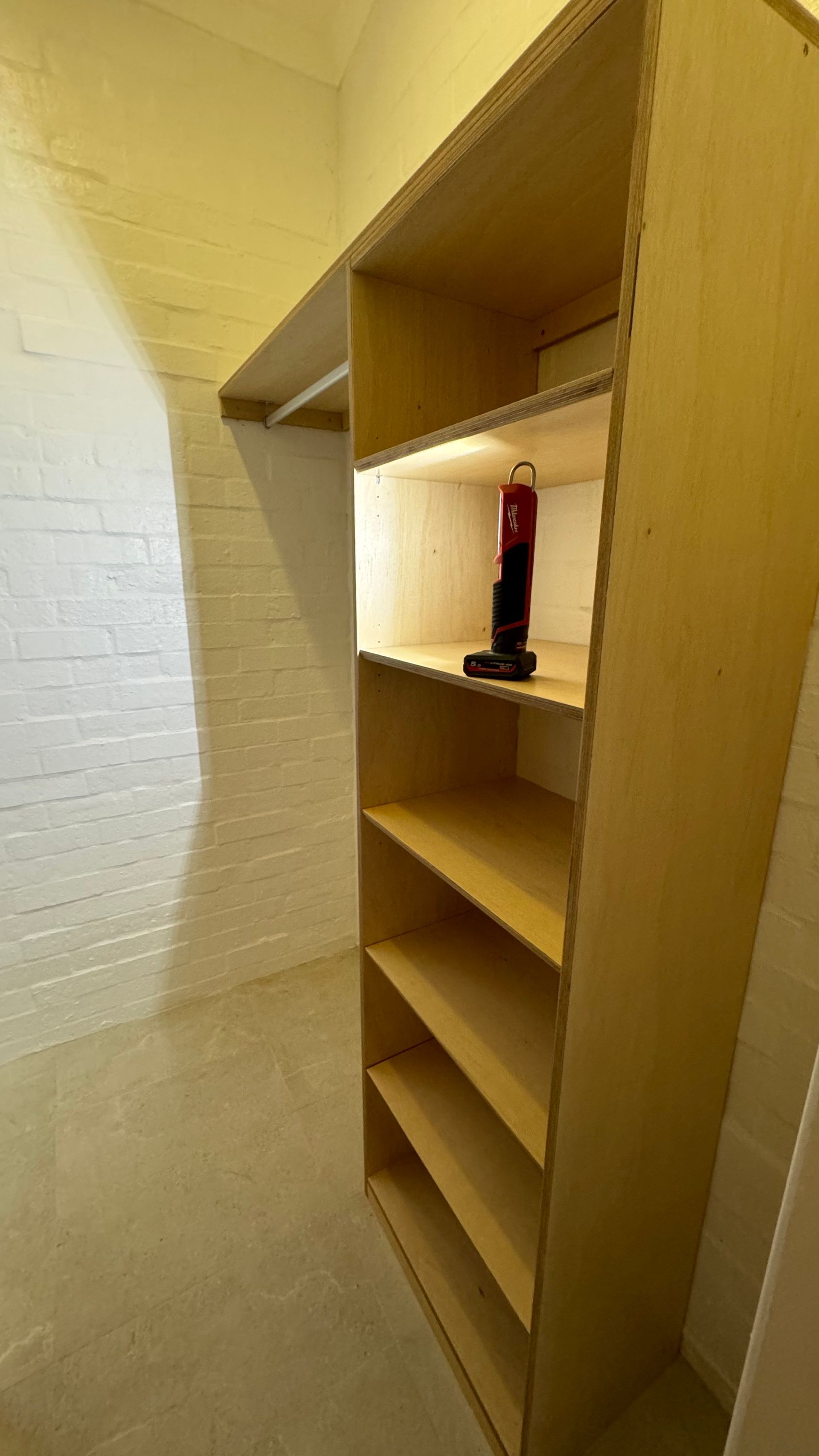 A walk in closet with wooden shelves and a light on the shelf — Coastal Detail Joinery in Tuncurry, NSW