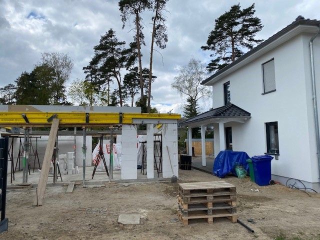 Bau eines Backsteingebäudes; Arbeiter montieren auf dem Dach Holzpaneele. Sonniger Tag, blauer Himmel.