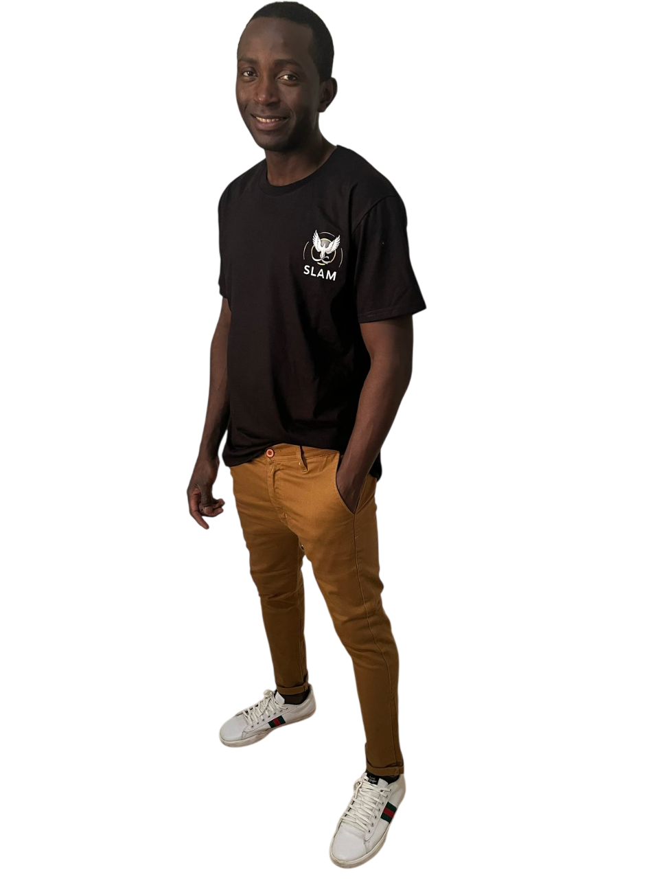 Hombre con una camiseta naranja y jeans rotos, con las manos en los bolsillos, de pie y con una expresión neutra.