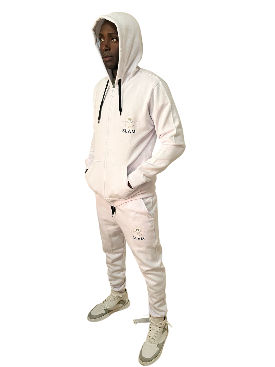 Persona con chándal blanco con capucha y las manos en los bolsillos. Zapatillas grises. Fondo blanco.