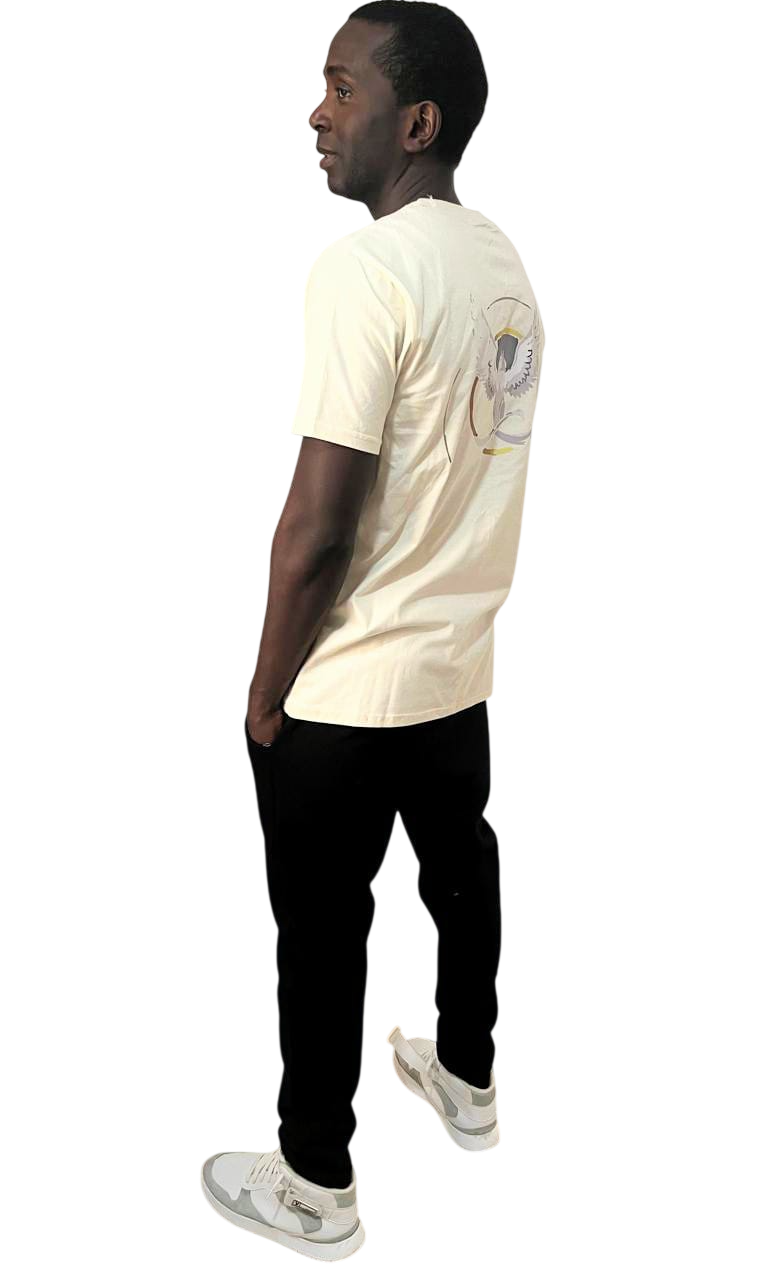 Hombre con camiseta color crema y pantalón negro, con las manos en los bolsillos, de pie y sonriendo.