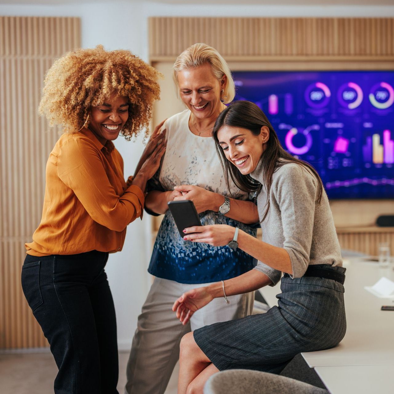 three women are looking at a cell phone together discussing UPS systems for their renewable energy office