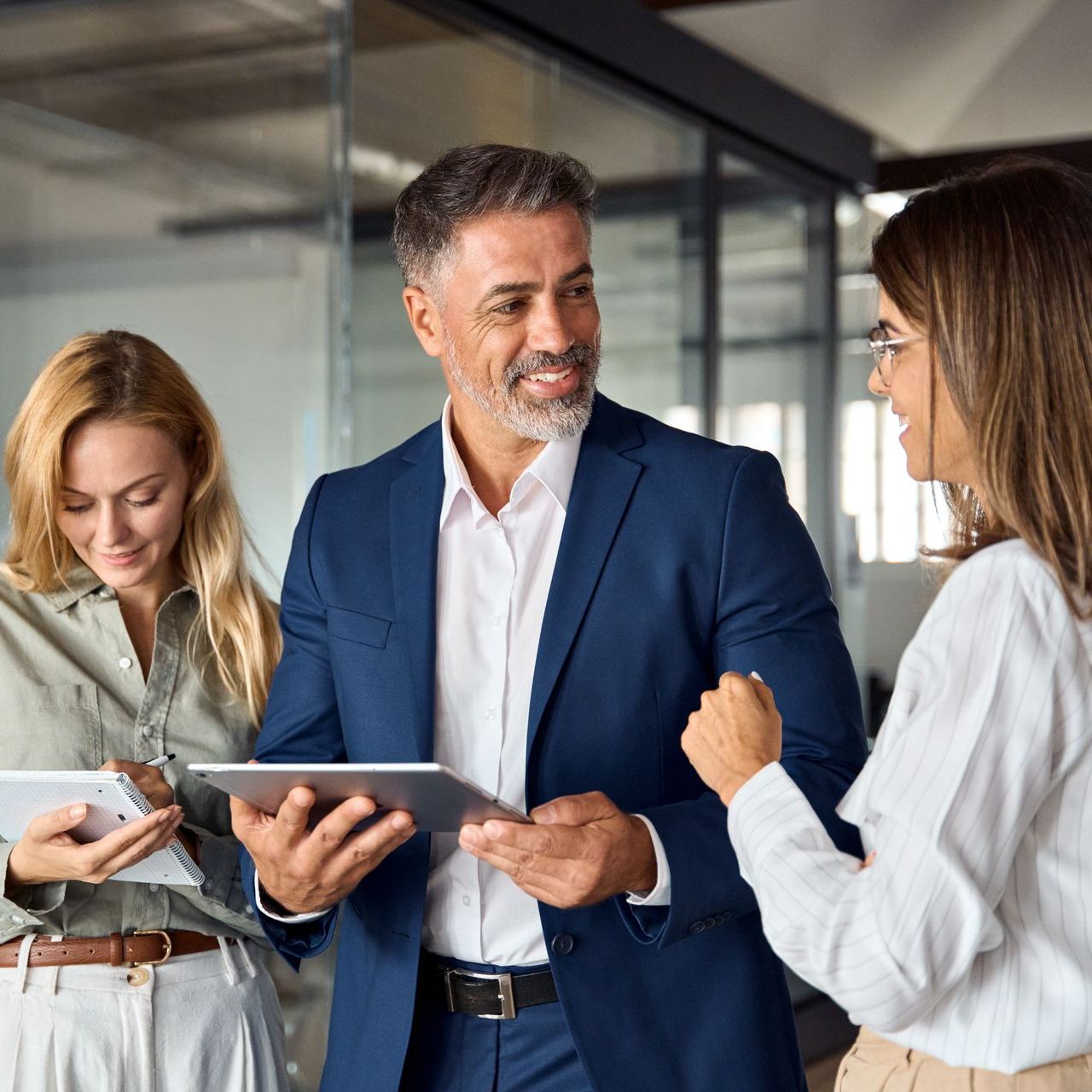 A man in a suit is talking to two women while holding a tablet.