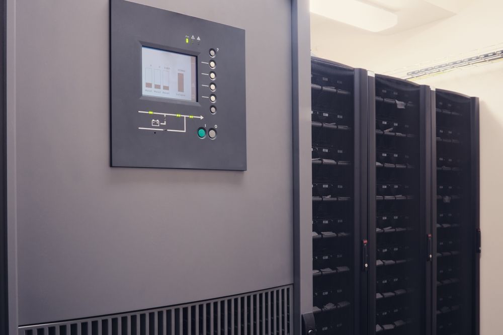 A server room with a row of servers and a control panel on the wall.