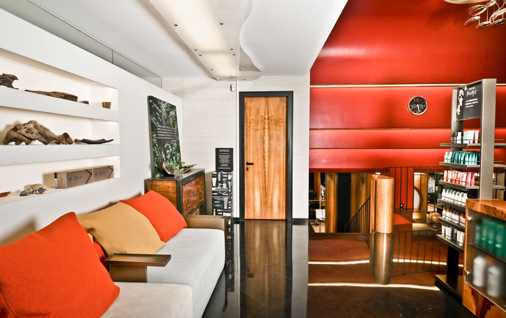 Una moderna sala d'attesa con un divano e cuscini arancioni, pavimento nero e una parete rossa.