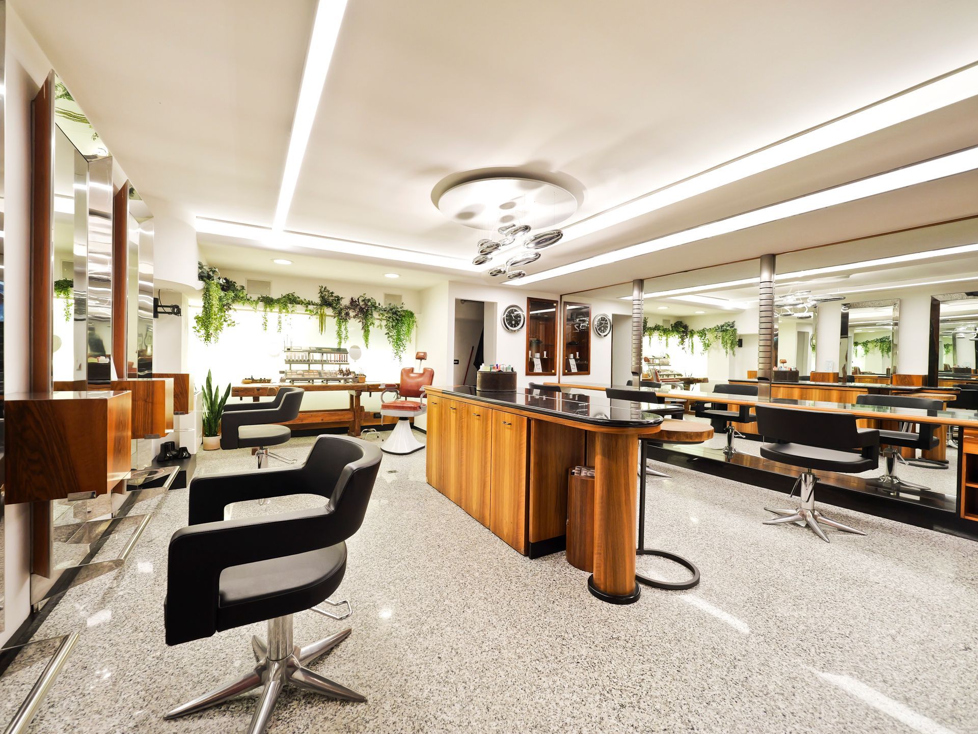 Interno di un salone da parrucchiere con postazioni per lo styling, specchi e pavimento in terrazzo.