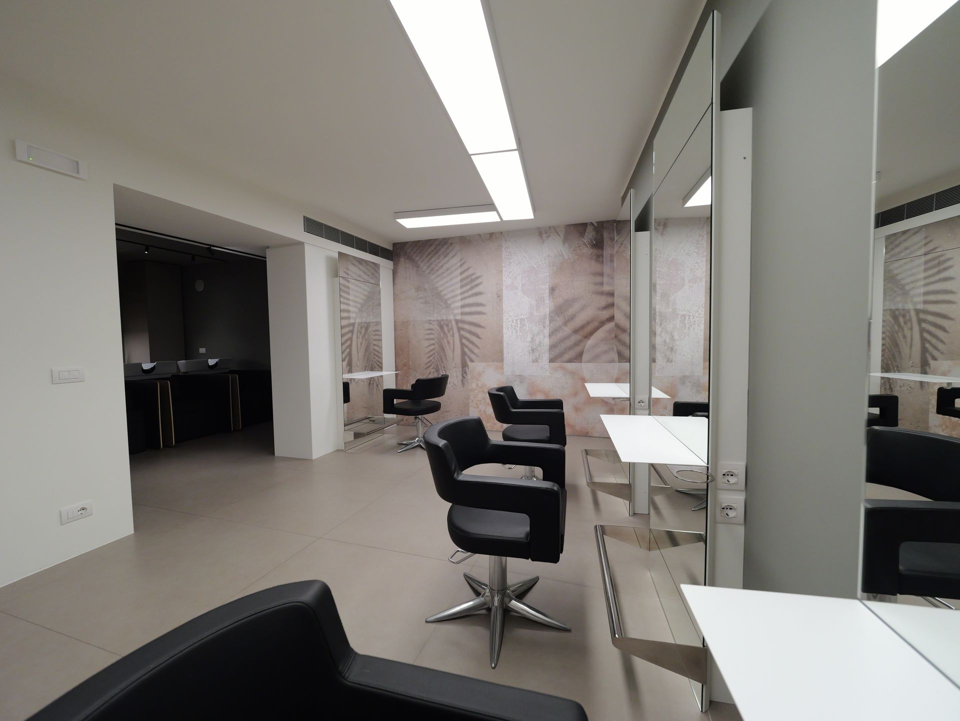Interno di un salone da parrucchiere con poltrone, specchi e quadri alle pareti dai toni neutri.