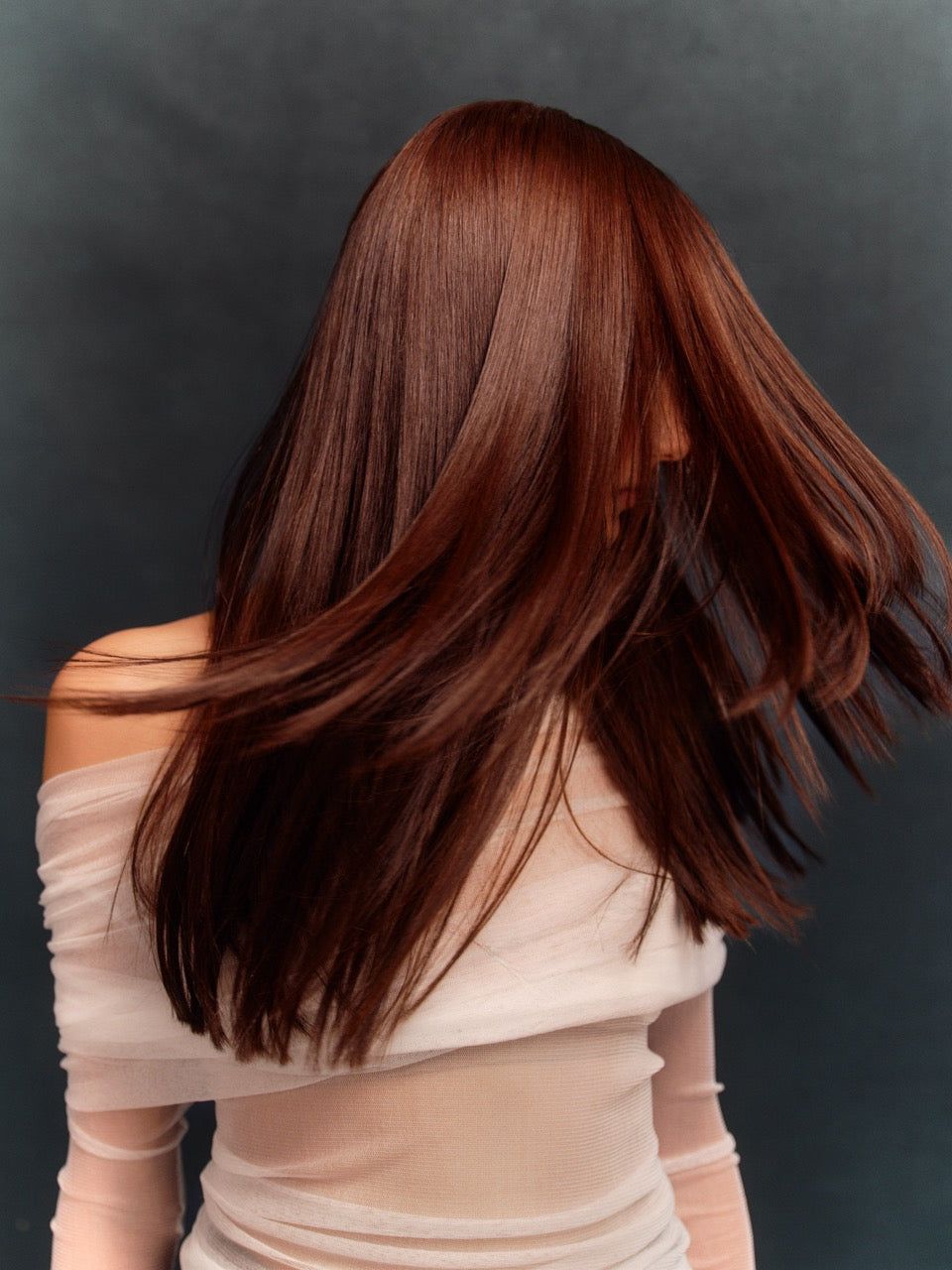 Donna con lunghi capelli castano-rossicci, indossa un top bianco con le spalle scoperte, capelli fluenti, sfondo scuro.