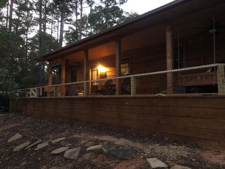 A wooden cabin with a covered deck and porch swing lit by interior lights at dusk in a forest setting.