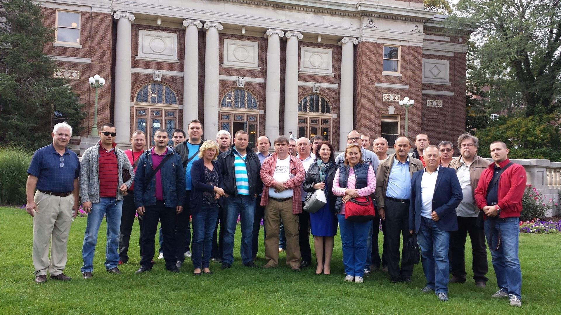 Group of people posing in front of a brick building with columns. Outdoors on a lawn.