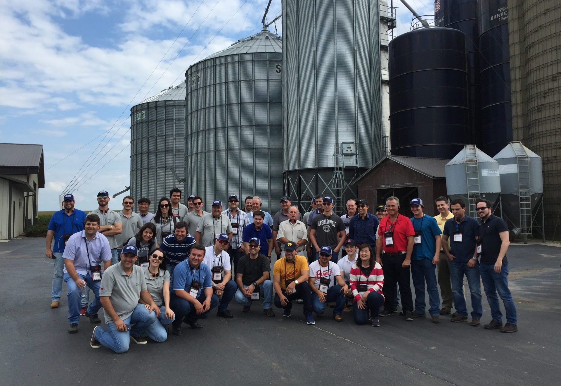 Group of people posing in front of grain silos on a sunny day.