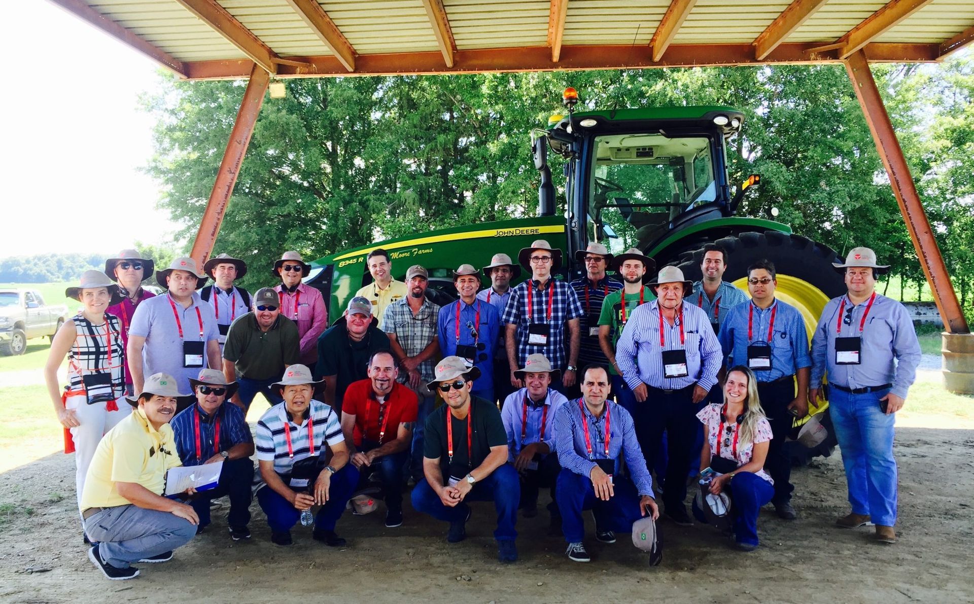 Group of people posing with a John Deere tractor under a wooden shelter.