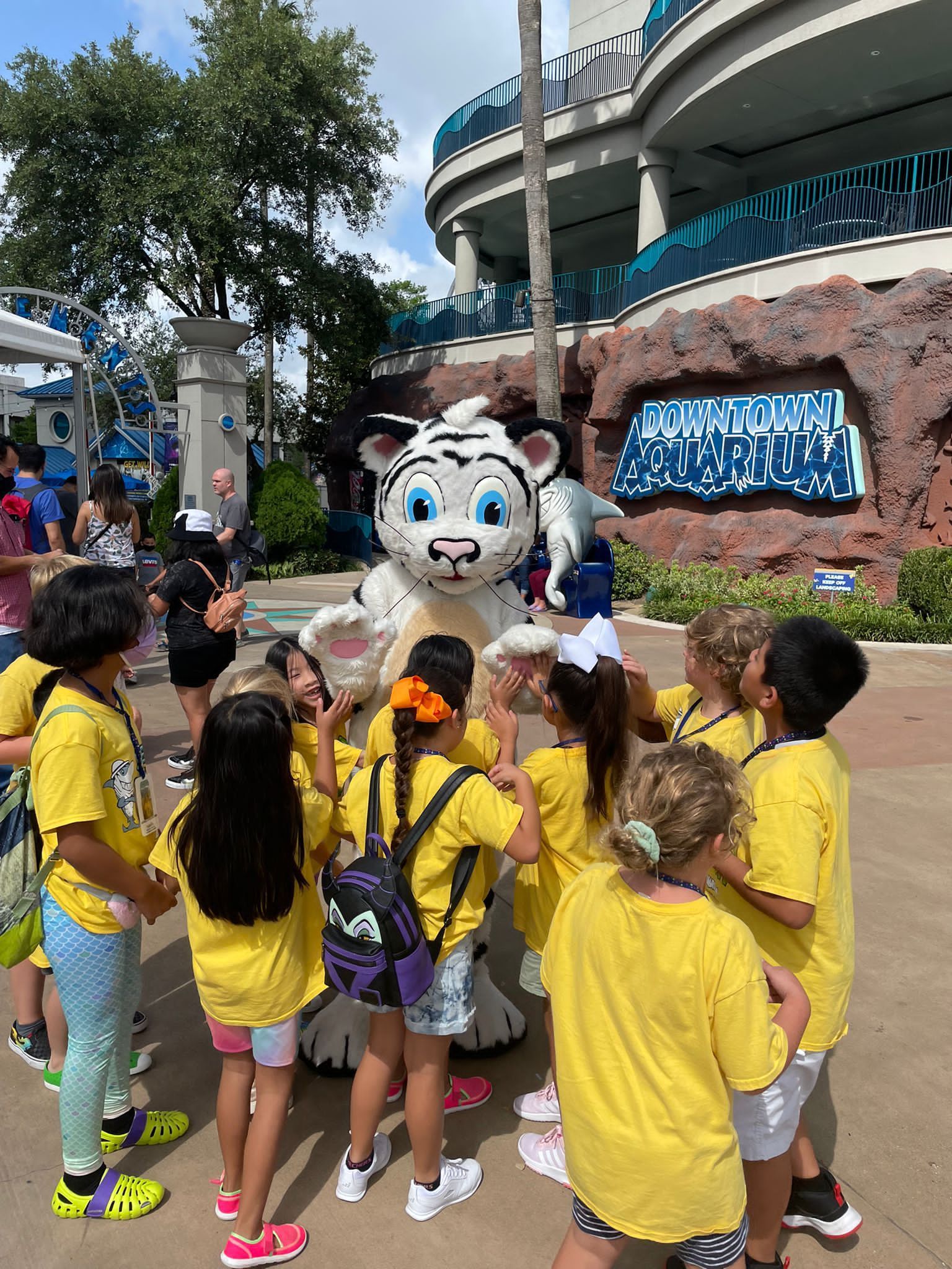 A group of children in yellow shirts are standing around a mascot