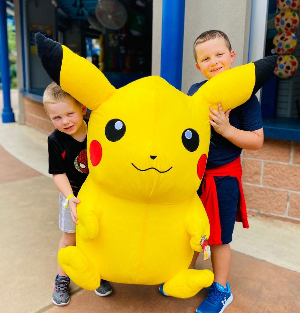 Two young boys standing next to a large stuffed pikachu