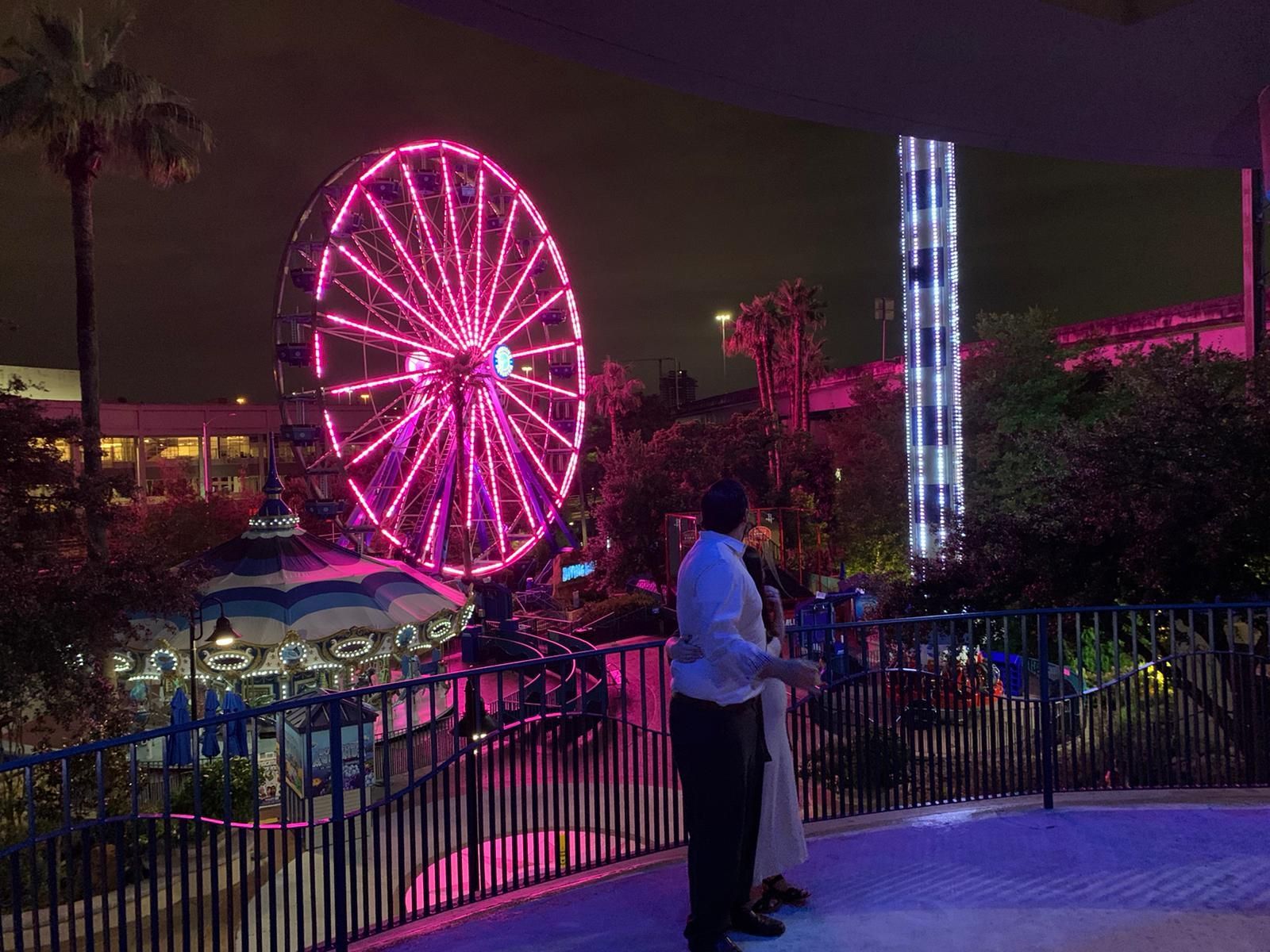 A couple standing in front of a ferris wheel at night that's pink