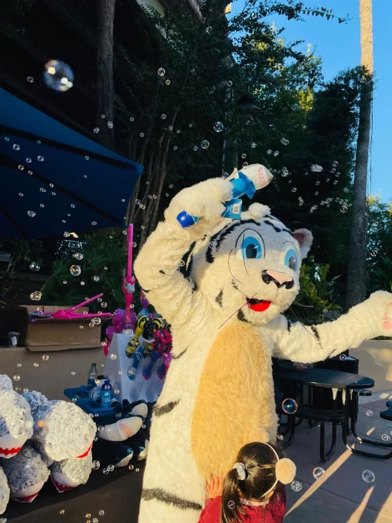 A little girl standing next to a tiger mascot blowing bubbles