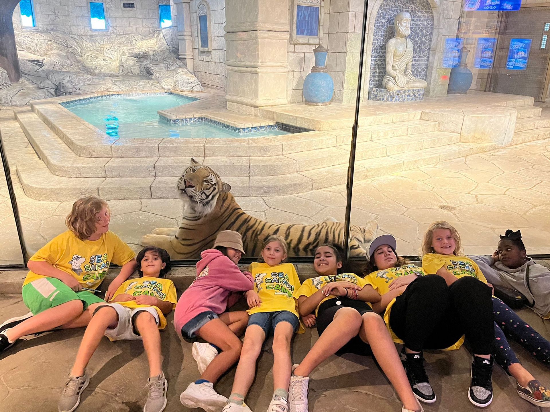 A group of children are sitting on the floor in front of a tiger.