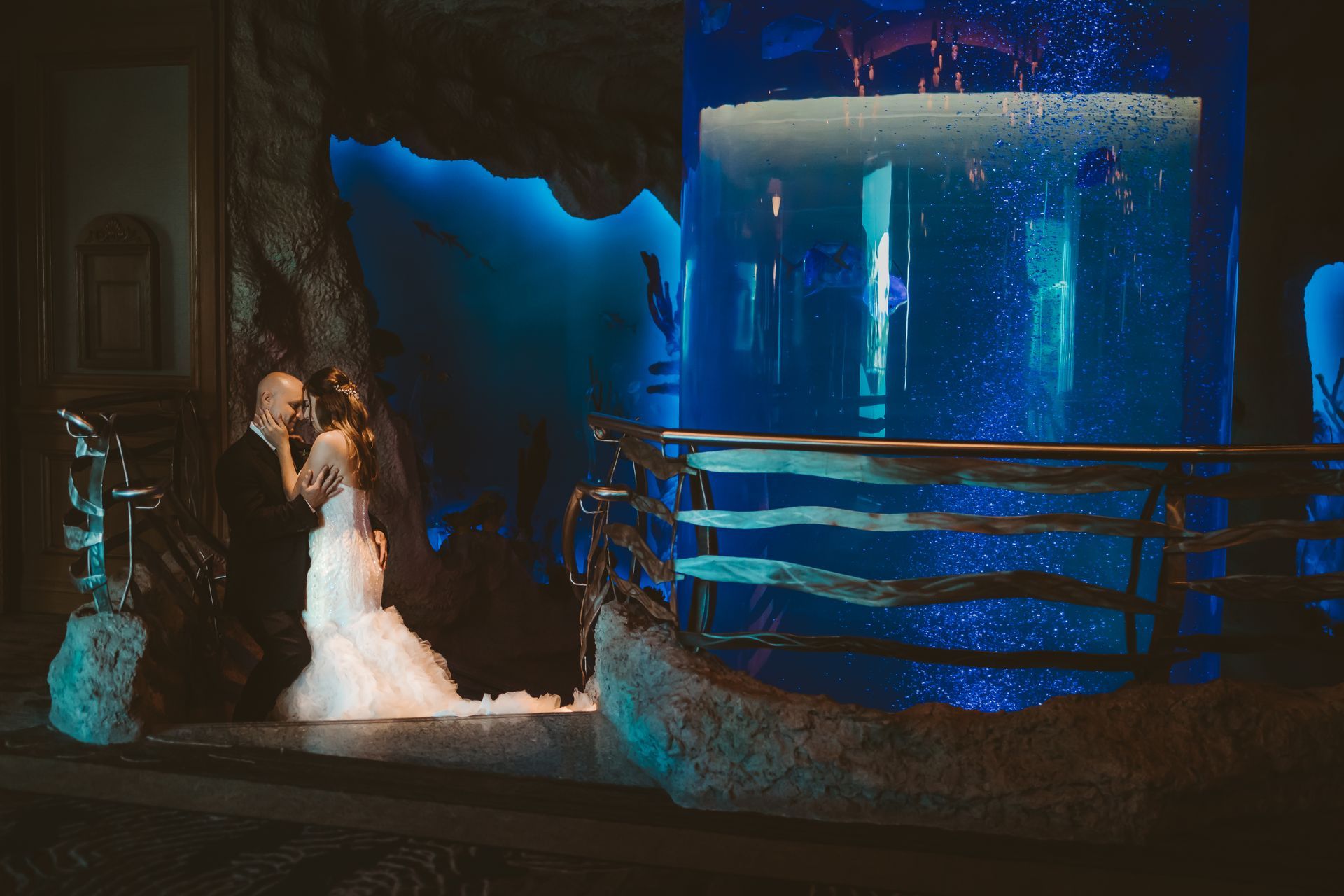 A bride and groom pose in front of an aquarium