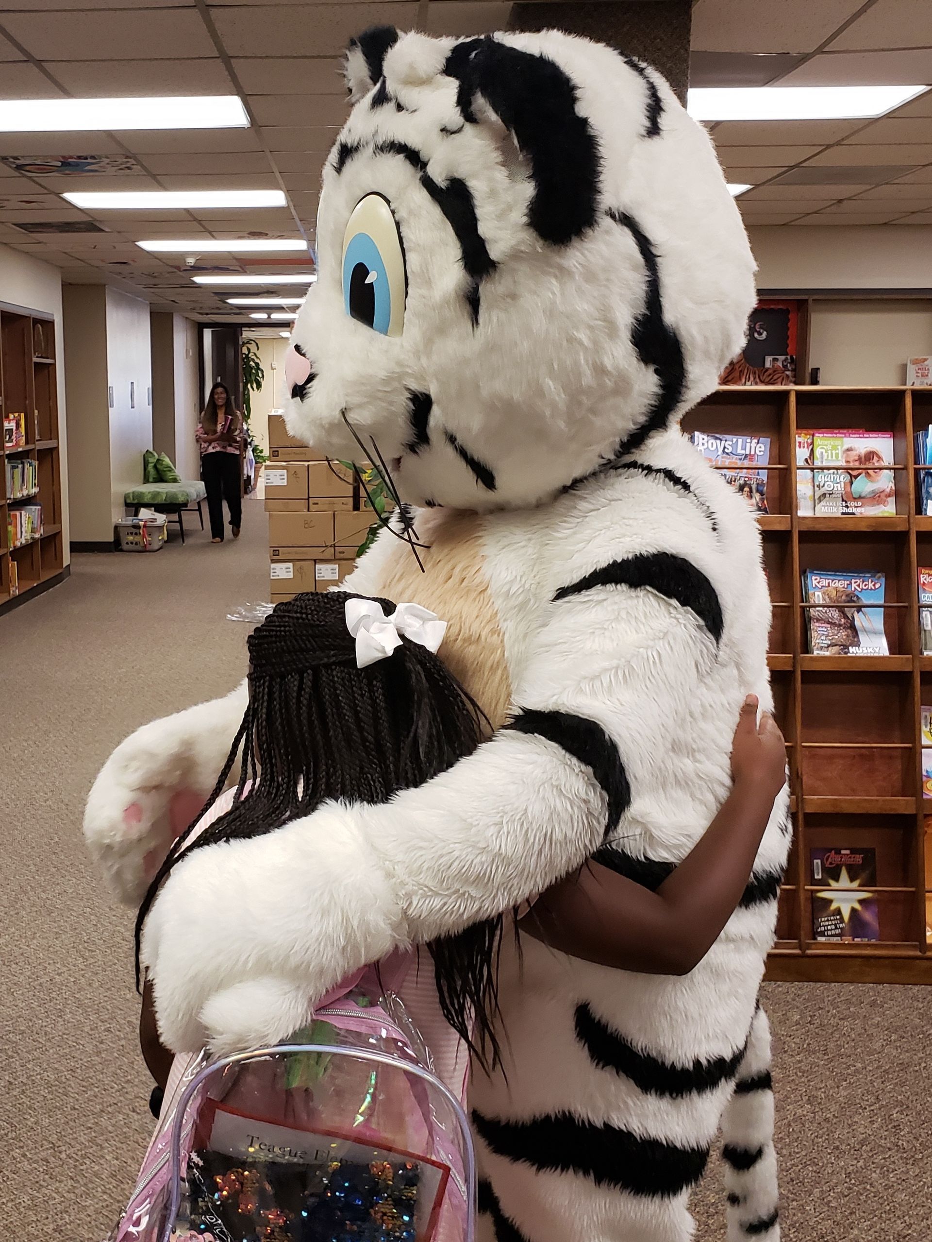 A mascot is hugging a little girl in a library