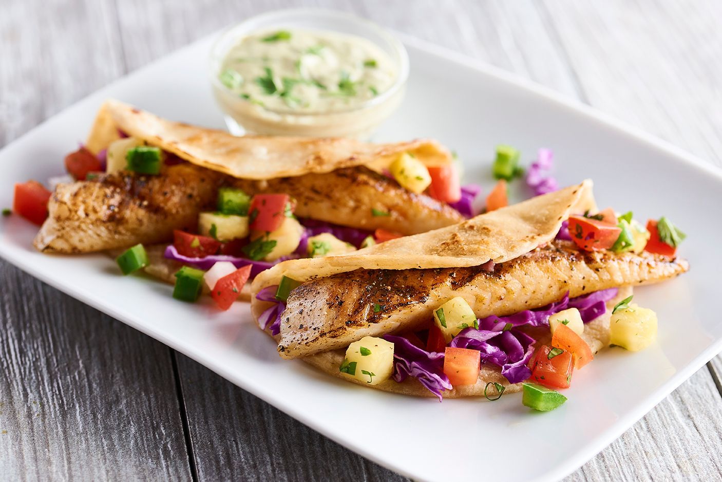 A white plate topped with fish tacos and vegetables