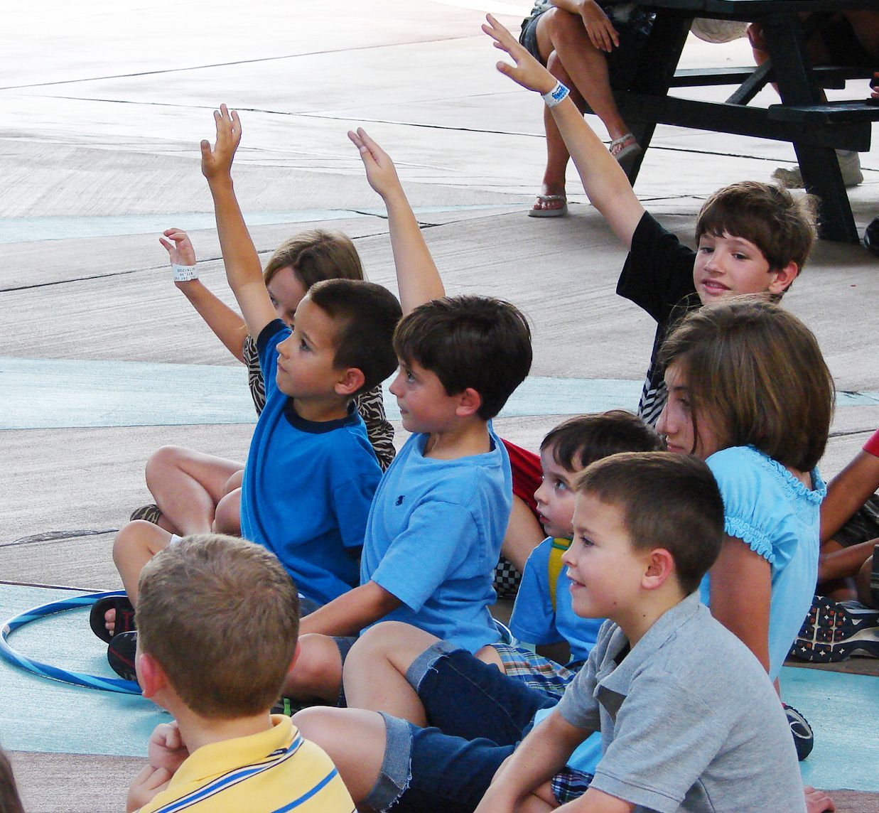 A group of children are sitting on the ground raising their hands