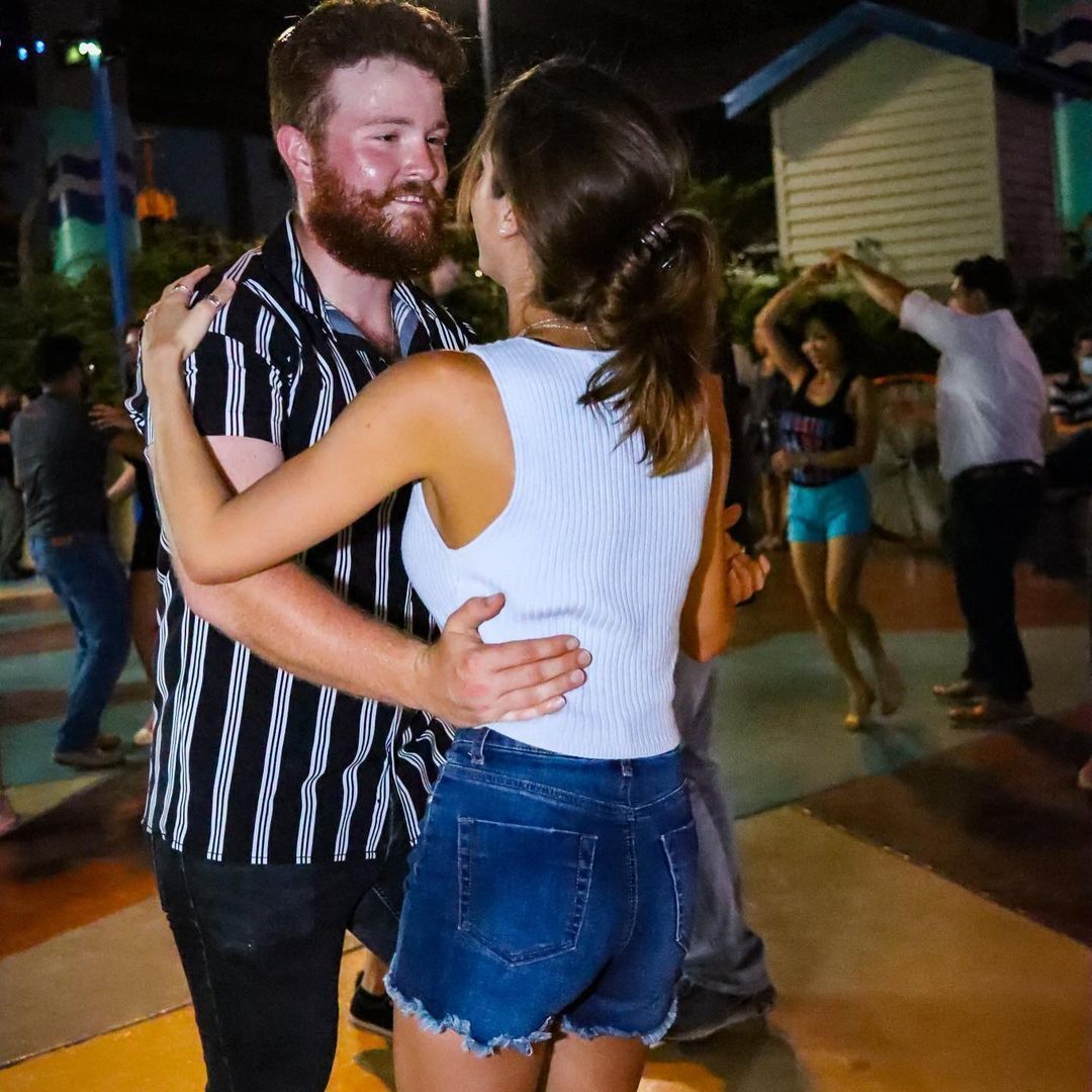 A man in a striped shirt is hugging a woman in shorts