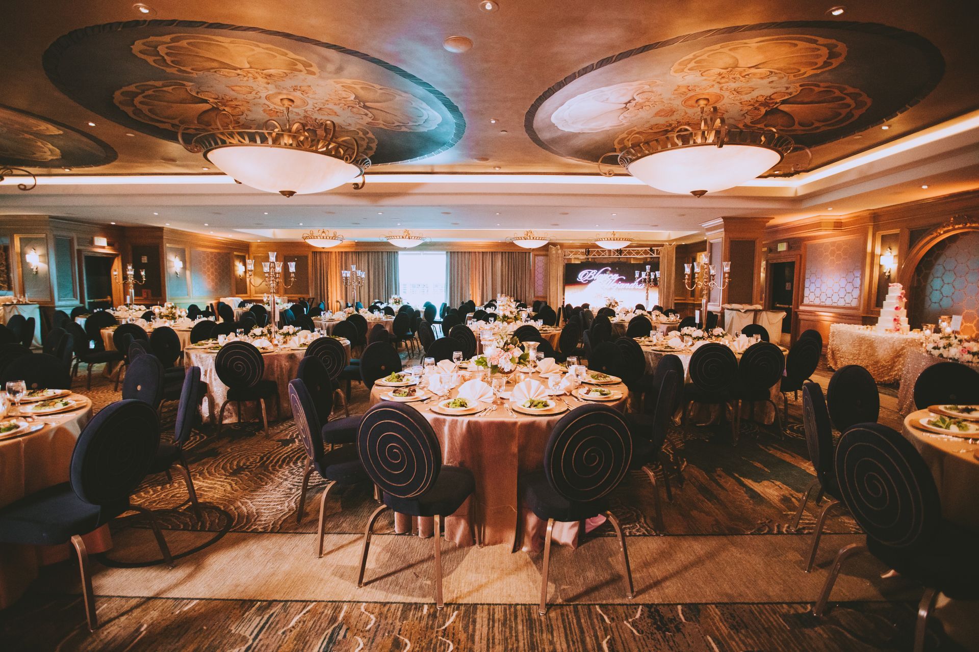 The Nautilus Ballroom, featuring round tables with gold tablecloths, dark chairs, and ornate ceiling chandeliers.